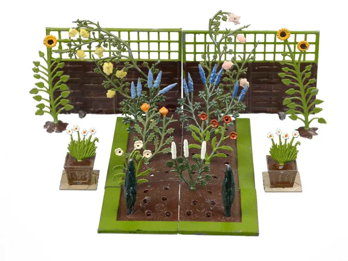 Miniature garden model featuring various plants, a flower bed, and a green fence, displayed on a white background.