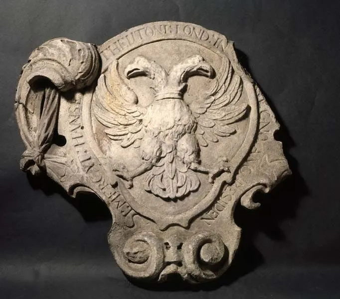 Ancient carved stone shield featuring a double-headed eagle and inscriptions, displayed against a dark background.