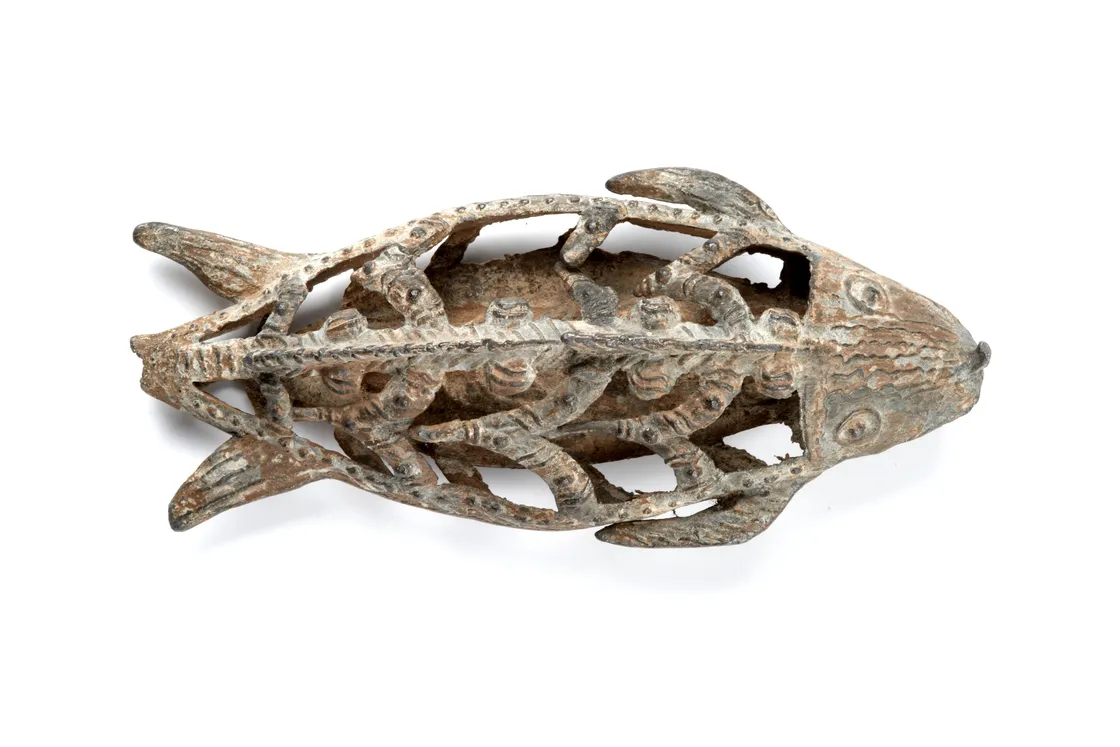 Carved fish-shaped object with an openwork design, featuring intricate patterns and organic shapes, photographed on a white background.