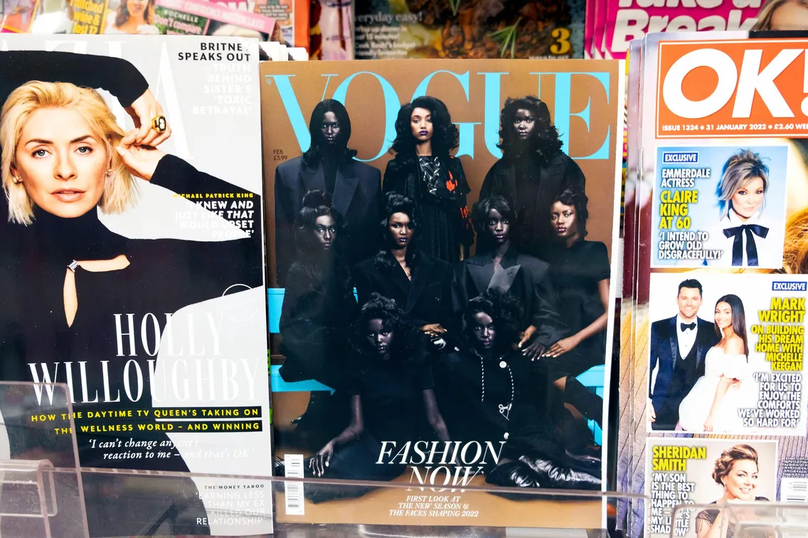 Magazines on display in a rack include Vogue, featuring models in black outfits, and others displaying various celebrity covers with headlines.
