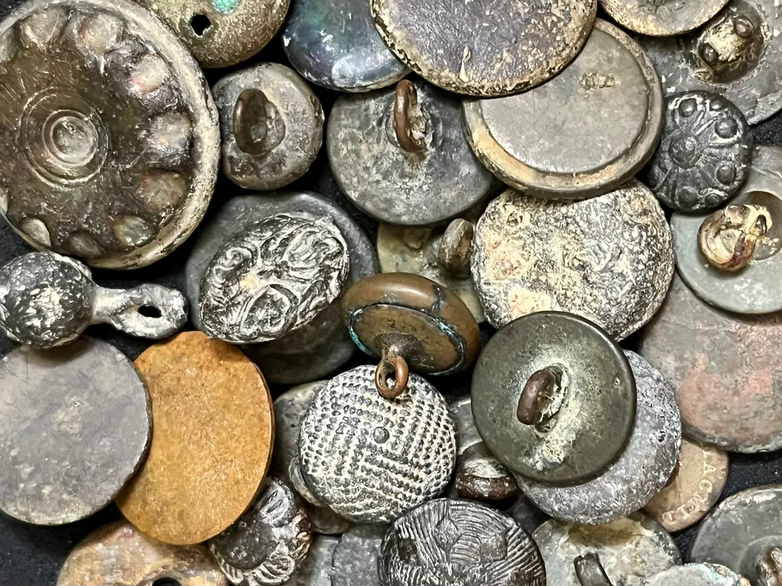 A close-up view of a pile of old, weathered metal coins and round tokens, some with intricate patterns and attached loops.