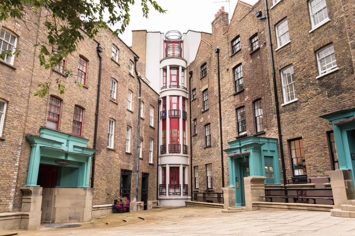 A courtyard surrounded by brown brick buildings with turquoise door frames and a central white building featuring red accents and circular windows.