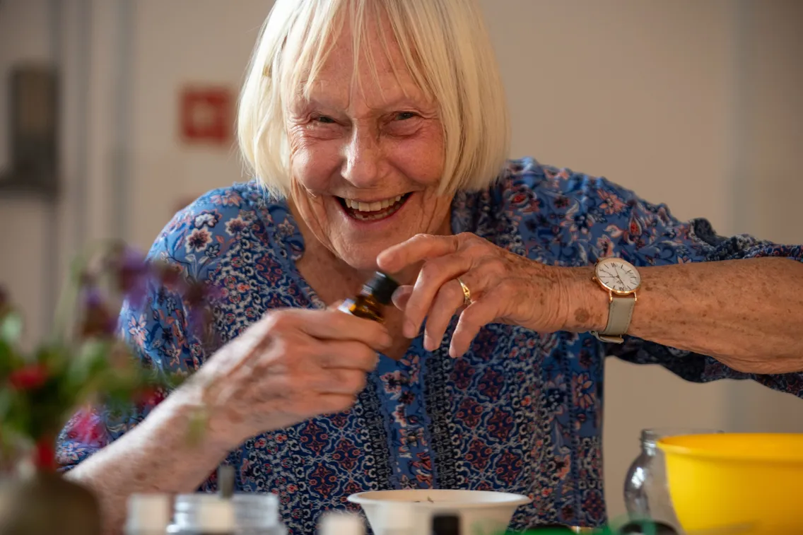 An older woman smiling at looking at the camera, while holding a bottle of essential oil.