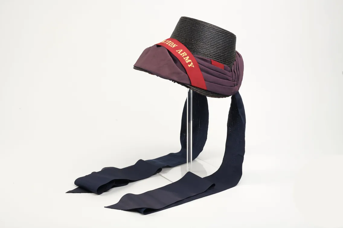 A black and maroon bonnet with a red "SALVATION ARMY" band and long navy blue ribbons displayed on a white background.
