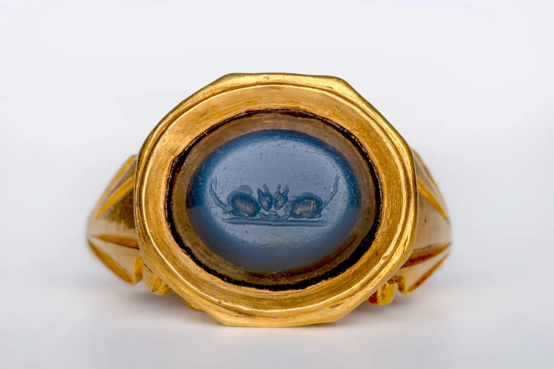 A gold ring featuring an oval blue gemstone with an engraving of two rabbits facing each other.