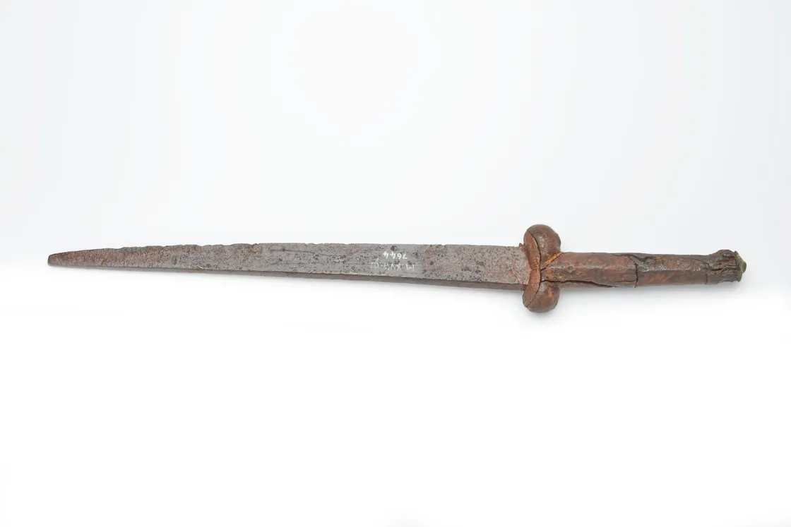 A rusty, ancient short sword with a straight double-edged blade and a corroded hilt against a plain white background.