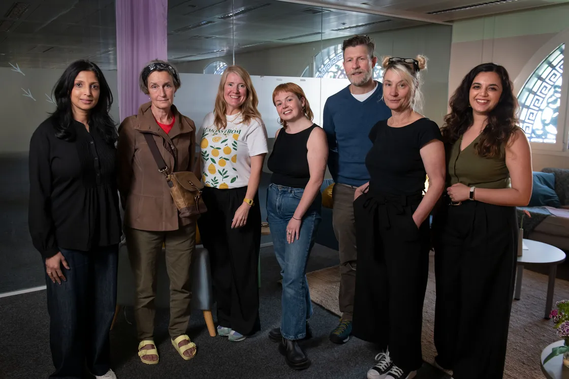 Seven people stood together in a room, facing the camera and smiling