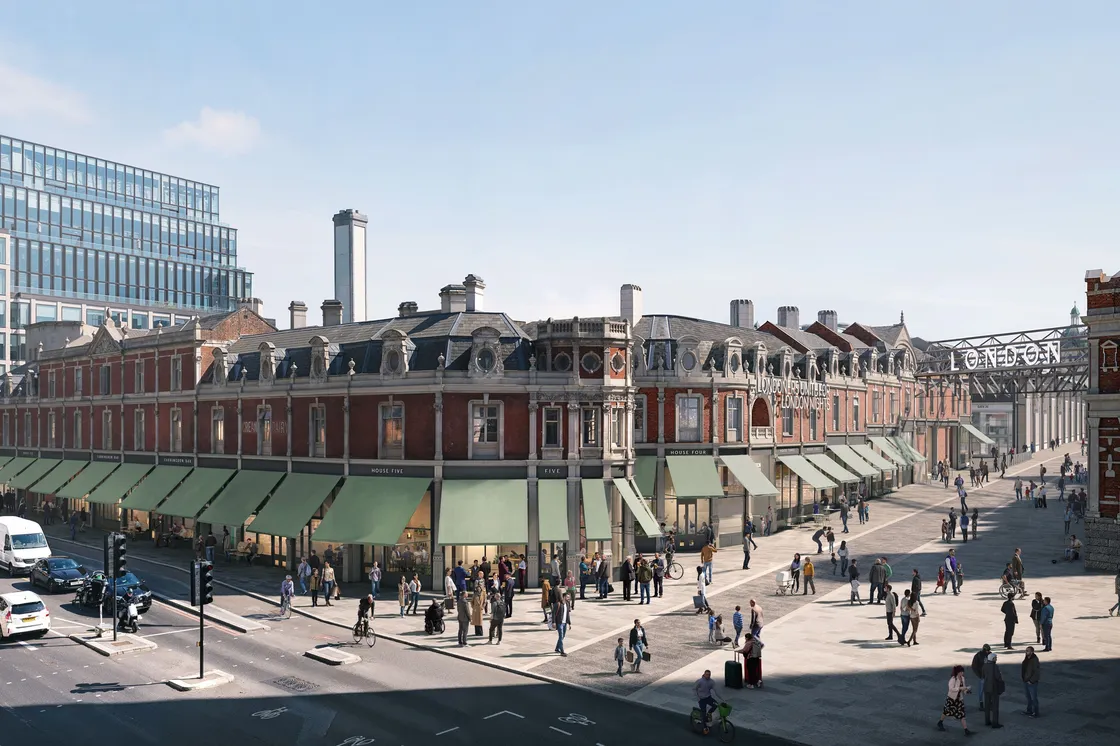 Street view of a historic brick building with green awnings, busy with pedestrians; modern glass offices and a metal footbridge visible in the background.