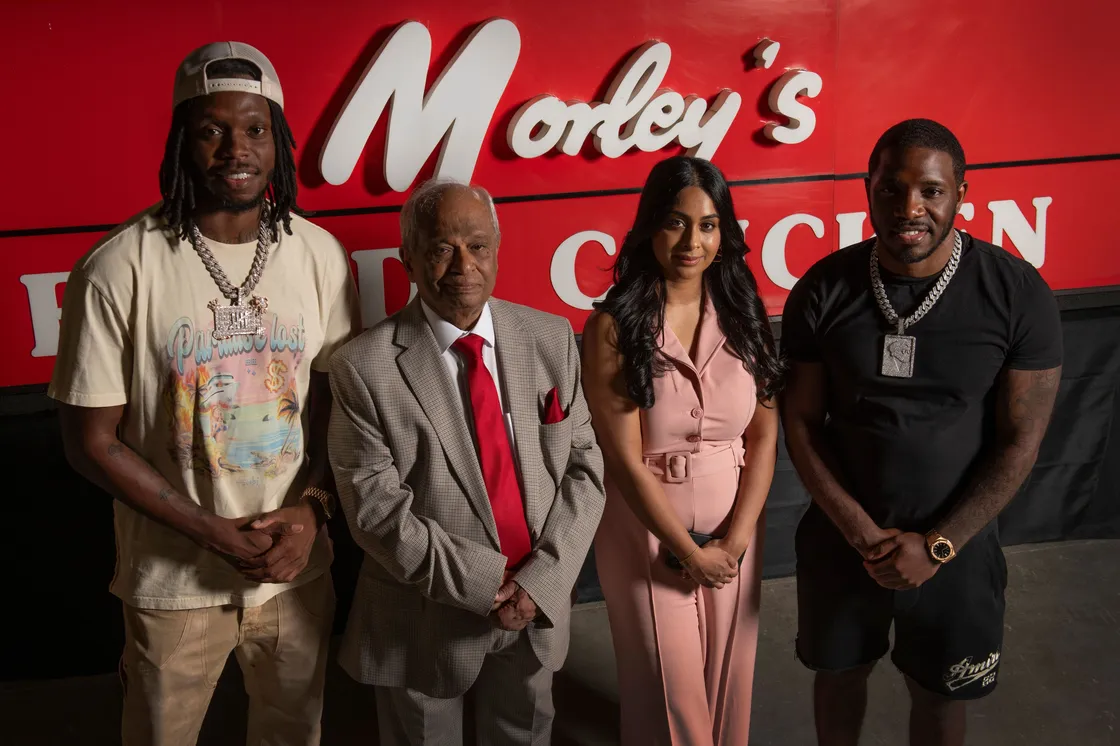 Four people stood in front of a red sign that reads "Morley's"