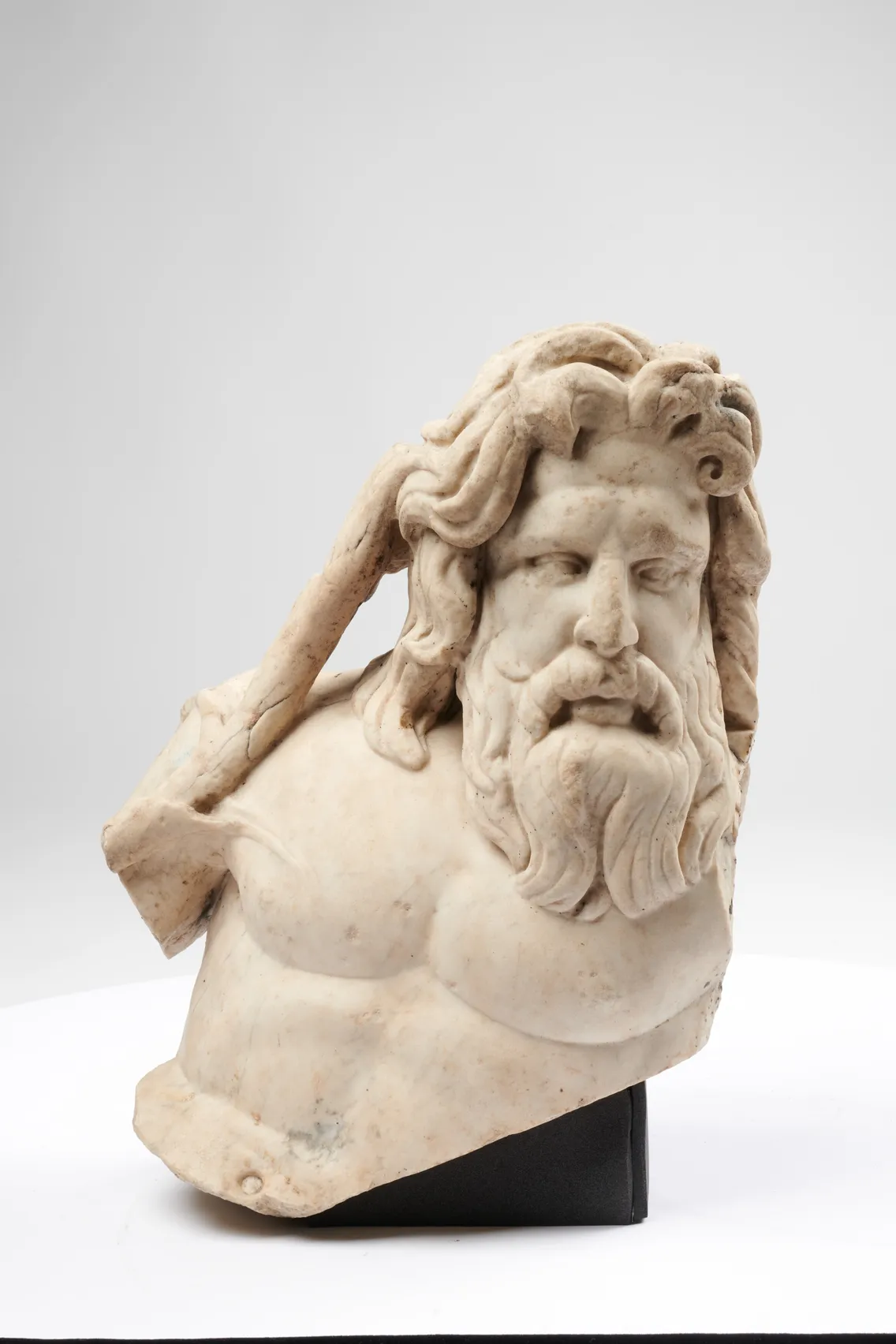 A marble bust depicts a bearded male figure with long hair and an intense expression, holding a staff or scepter over his left shoulder.