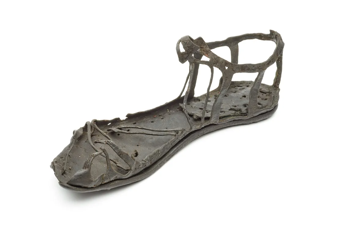 Ancient Roman leather sandal with intricate straps and a worn sole, displayed on a white background.