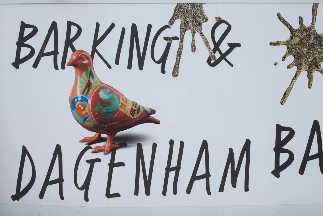 A colorful pigeon sculpture stands in front of a white wall with bold black text that reads "Barking & Dagenham.