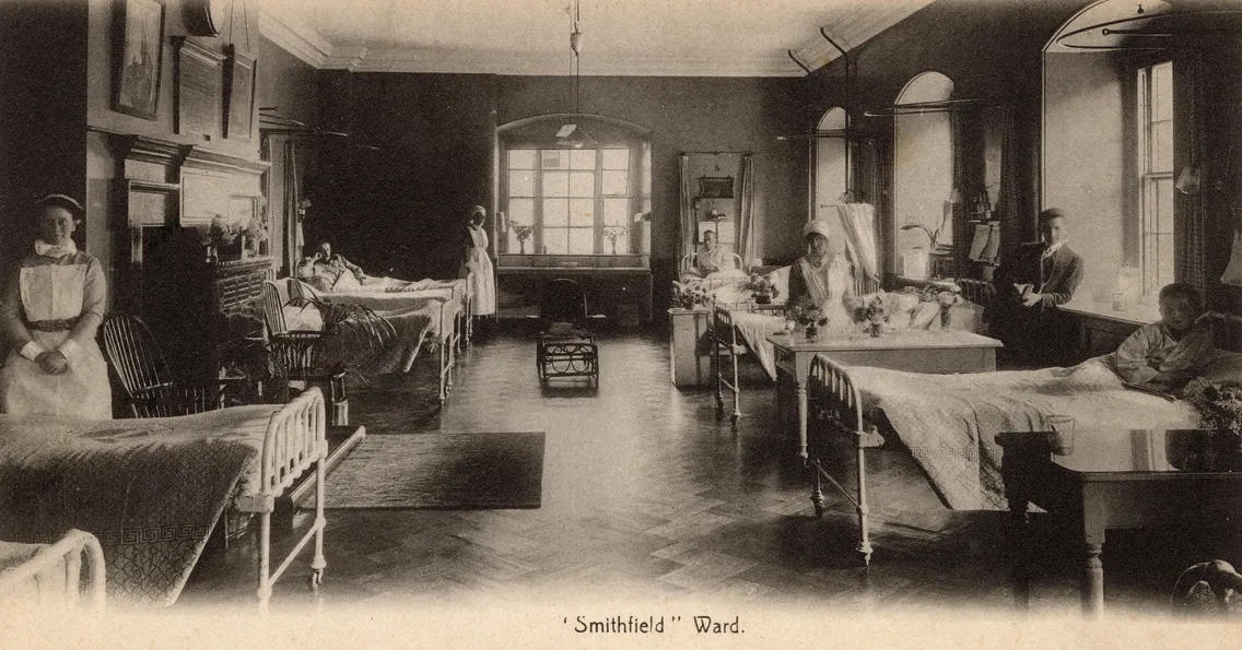 A vintage hospital ward with several beds, nurses in uniform, and patients resting; sunlight streams through large windows.