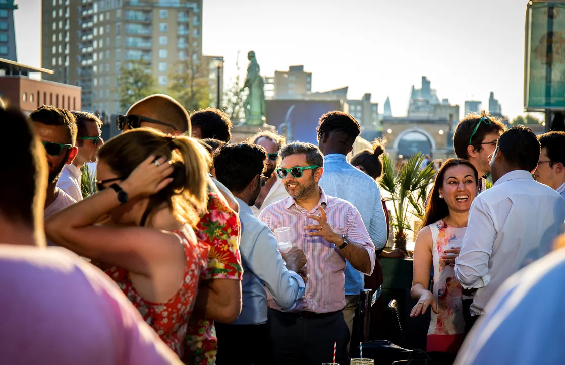 A group of people socializing at a rooftop gathering with city buildings in the background.