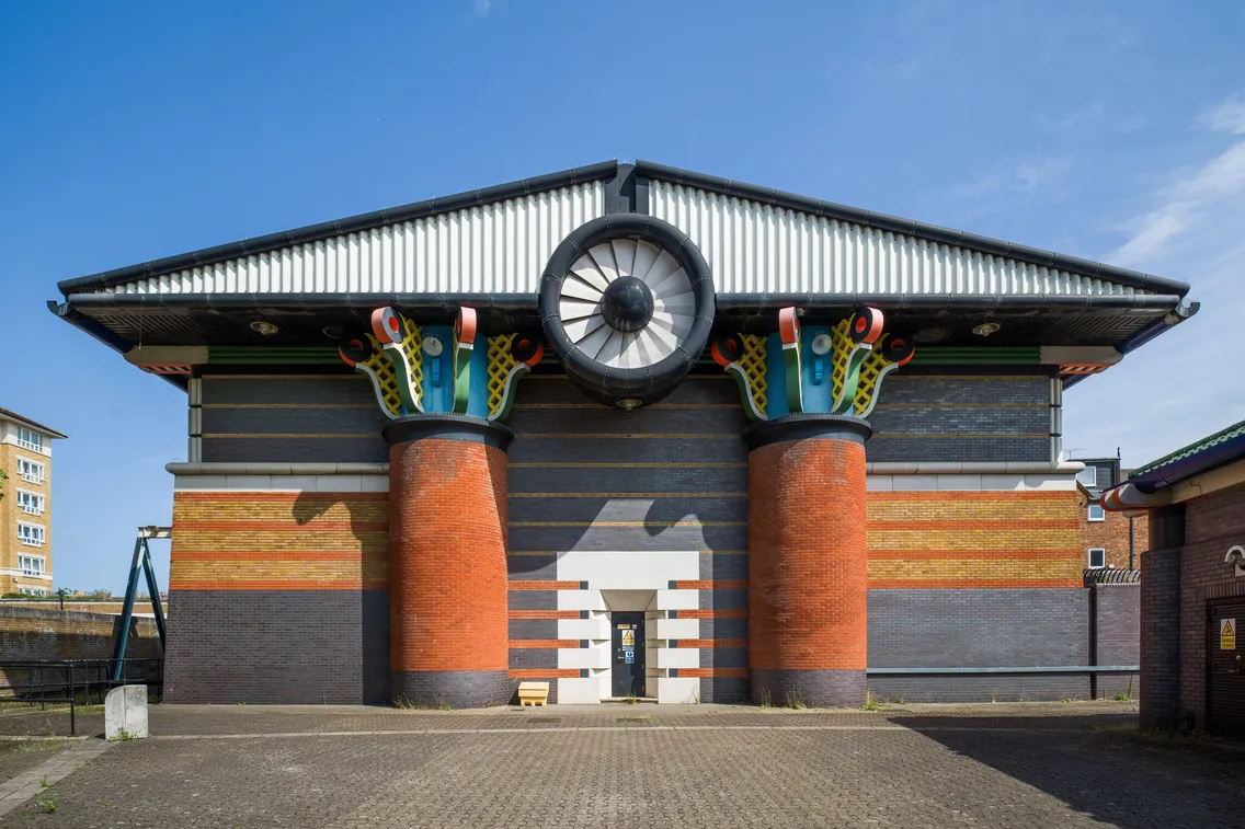 Front view of a colorful, industrial-style building with two large, cylindrical columns and decorative elements under a triangular roof.