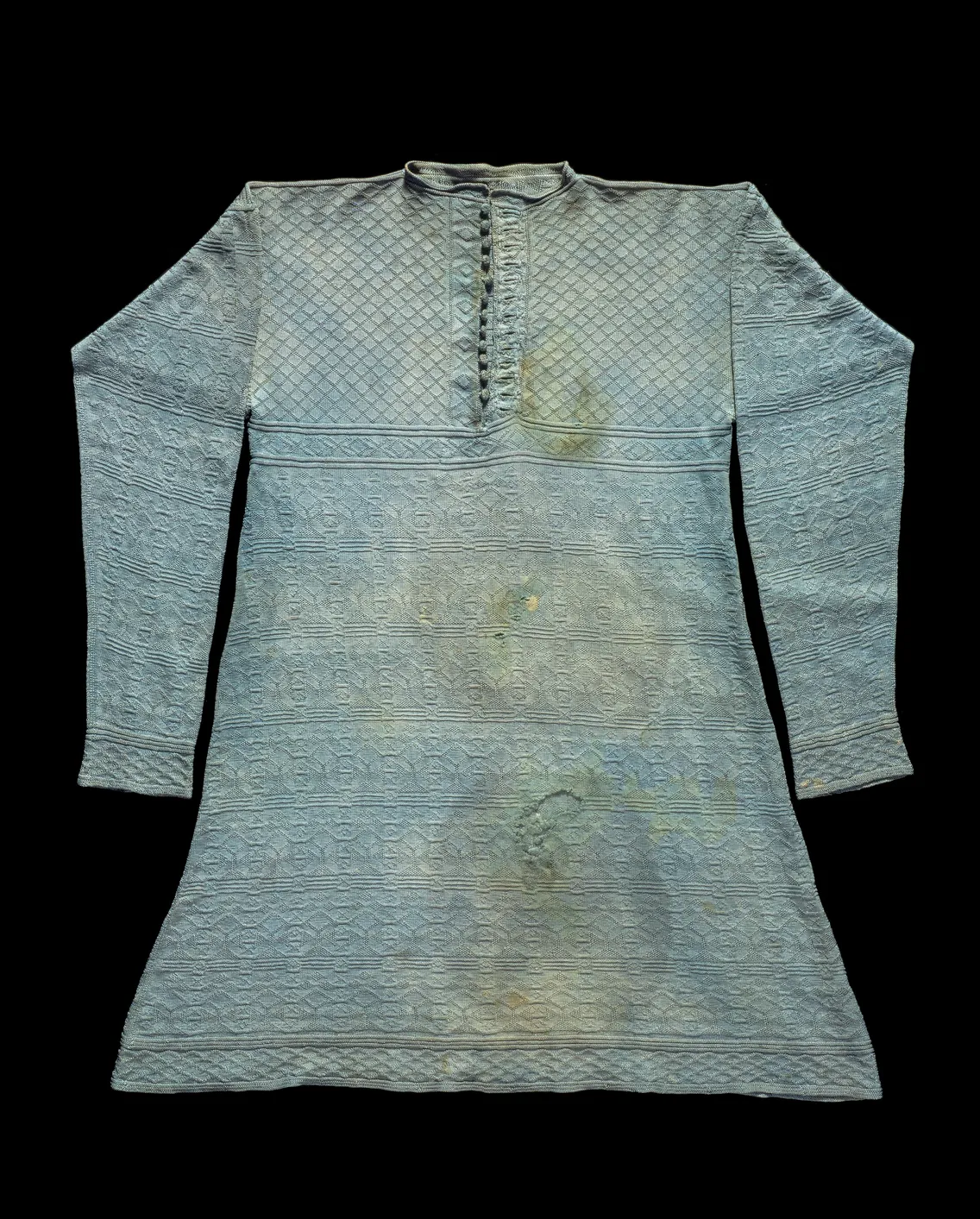 A traditional light blue robe with an intricate pattern, visible wear and staining, displayed against a black background.