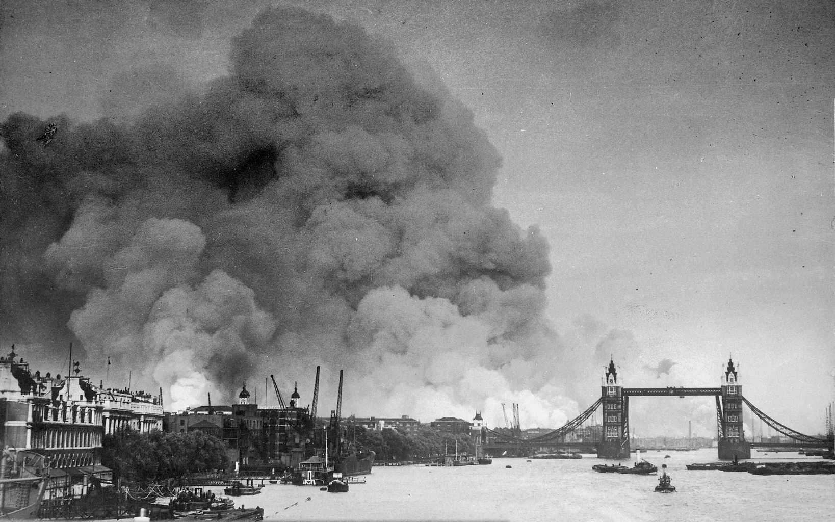 Black and white photo showing thick smoke over London during the Blitz, with the Tower Bridge prominently visible on the right side of the image.