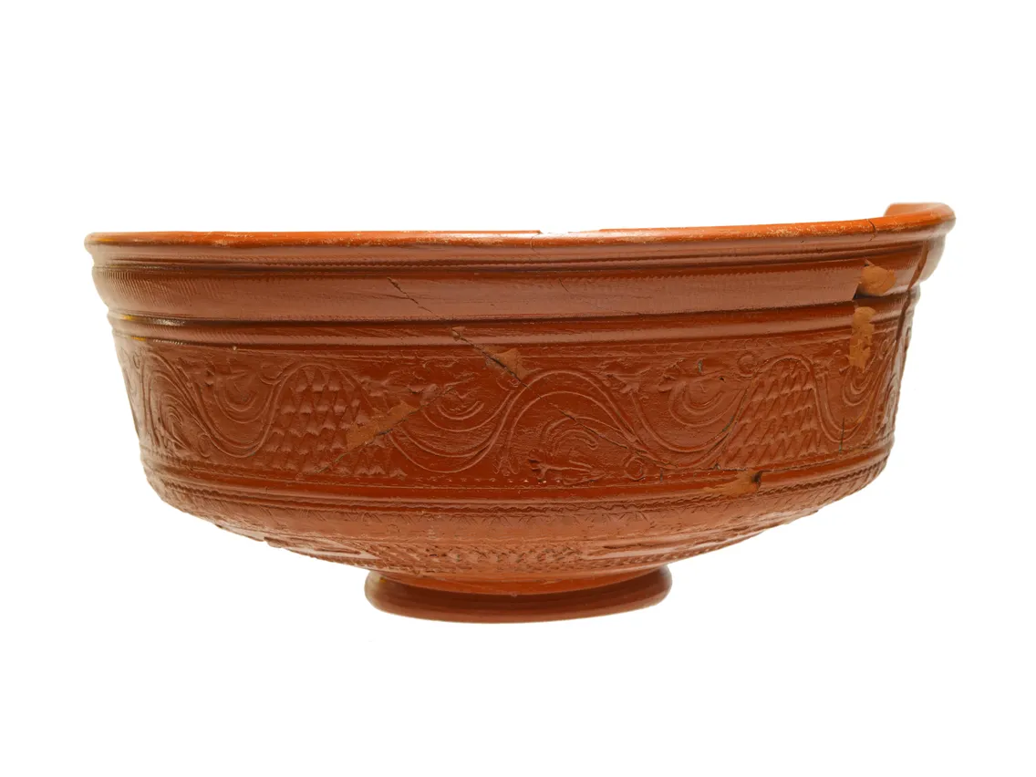 An ornate terracotta bowl with intricate carved designs, displayed against a white background.