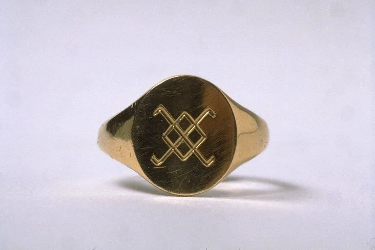 Gold signet ring featuring an engraved double "x" design on a plain background.
