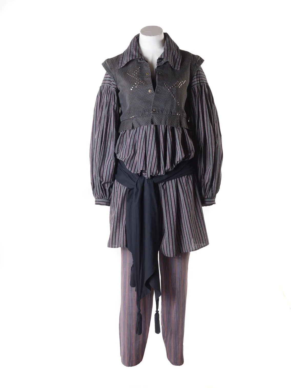 Mannequin displaying a striped avant-garde outfit with a studded vest and asymmetrical skirt, isolated on a white background.