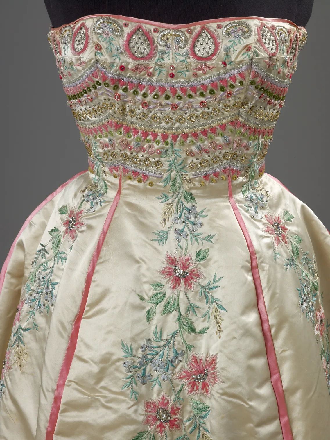 Detailed view of an elaborate embroidered dress with floral patterns and intricate beadwork on a mannequin.