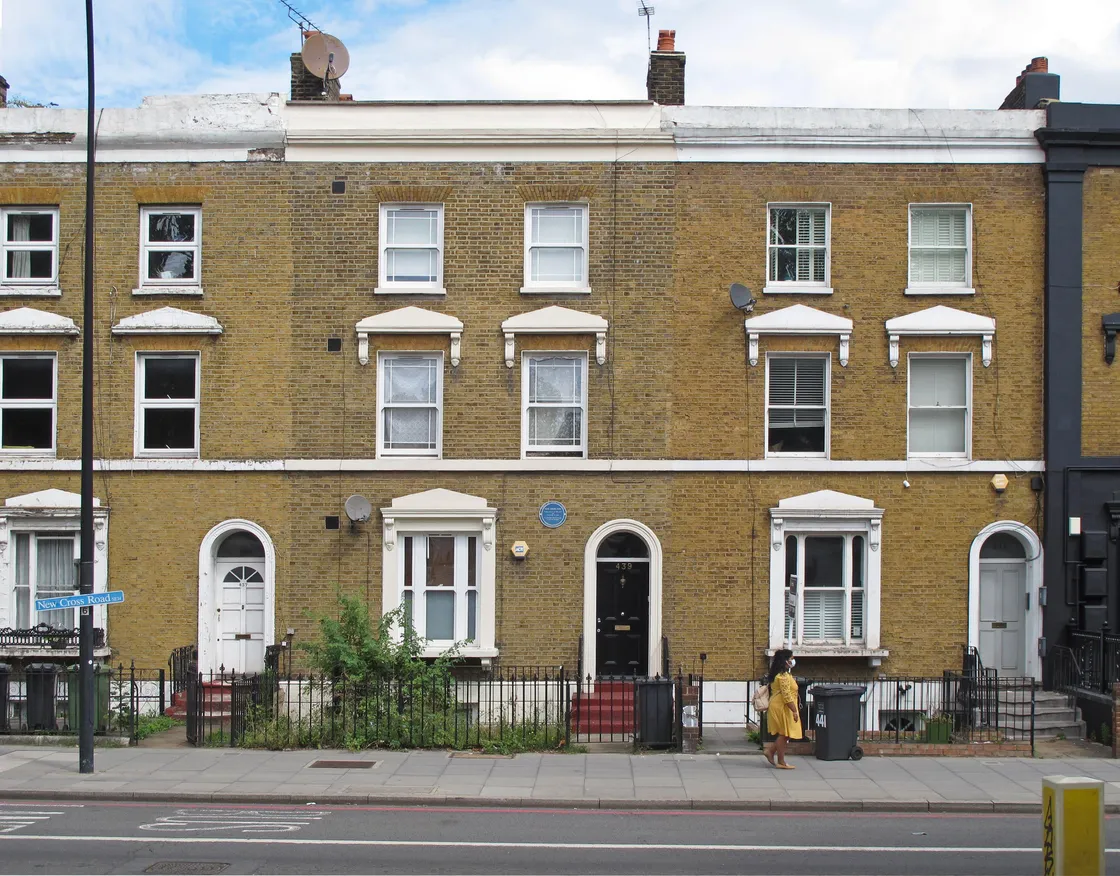 A row of four-story brown brick townhouses with arched doorways and white window frames. One person is walking on the sidewalk in the foreground.