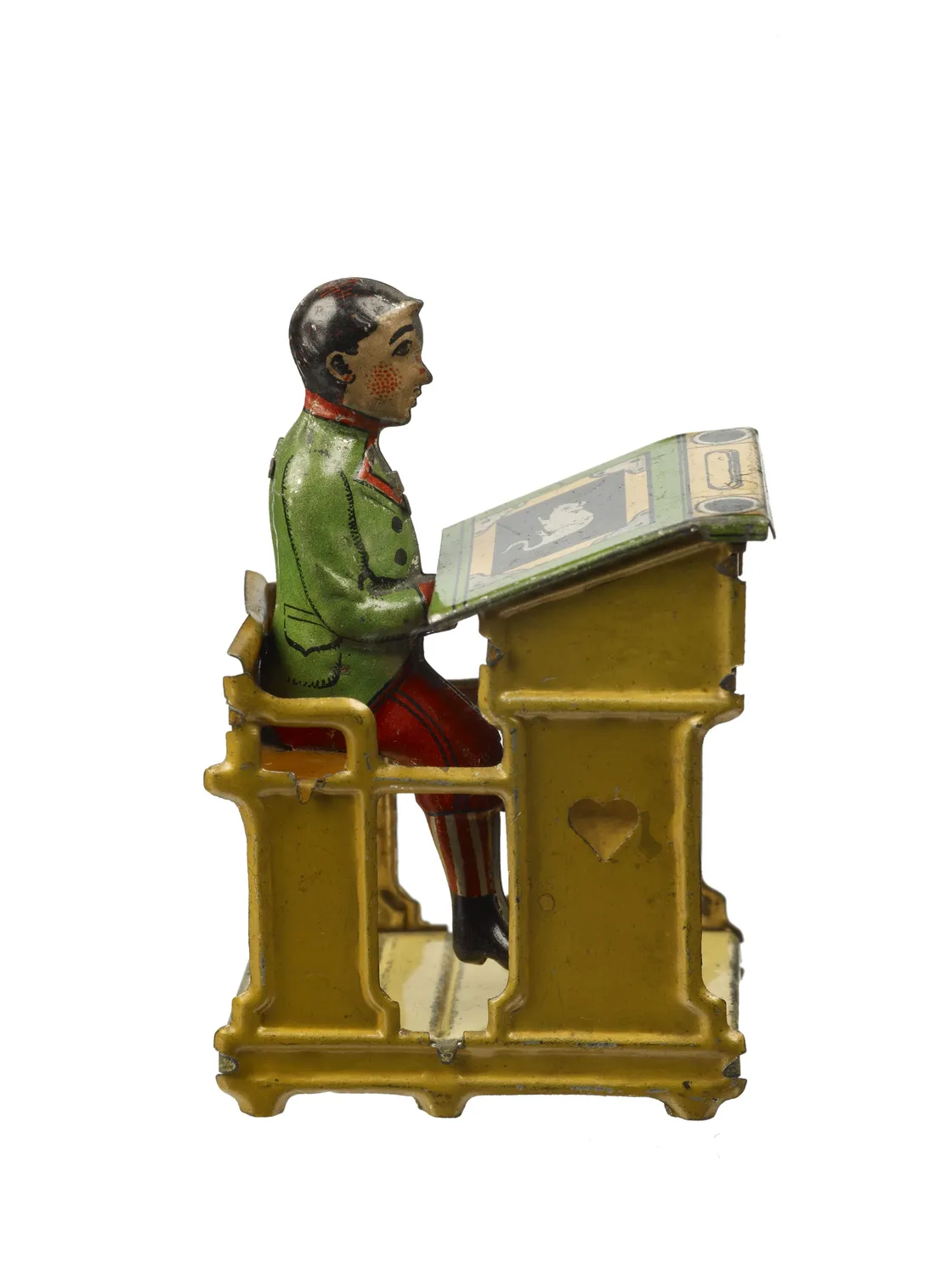 Vintage tin toy depicting a boy seated at a yellow desk, reading a book, in colorful attire. painted details and mechanical construction suggest early 20th-century manufacture.