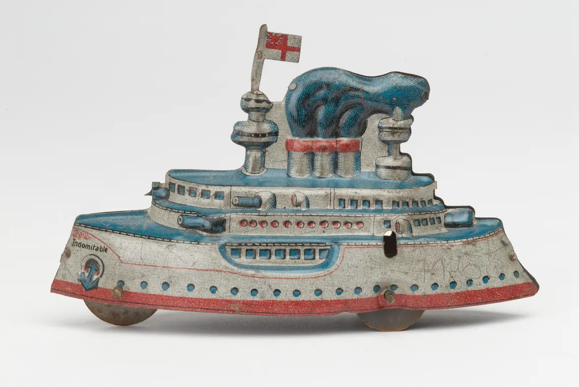 Vintage tin toy battleship with faded blue and red paint, featuring multiple gun turrets and a georgian flag, on a white background.