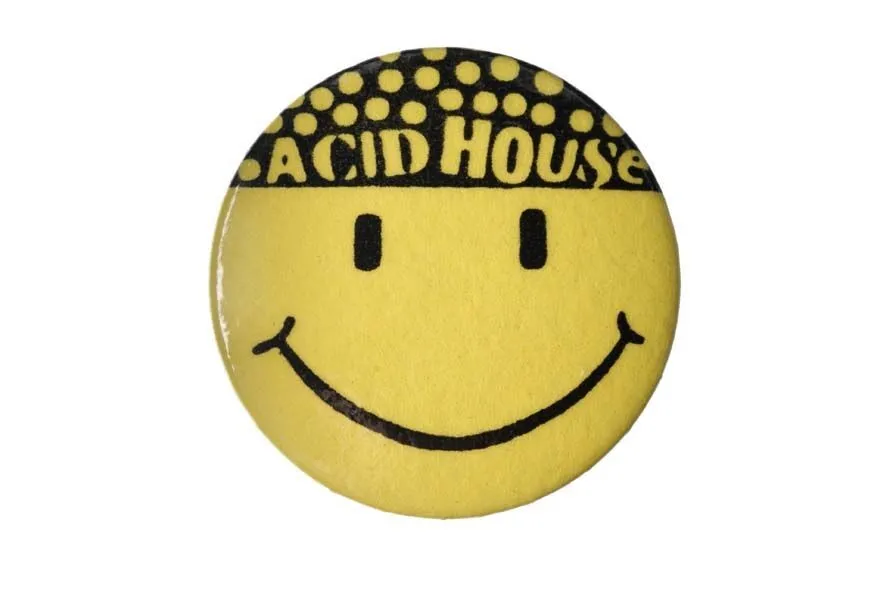 A yellow pin badge featuring a smiling face and the words "acid house" on top, styled with a white dot pattern.