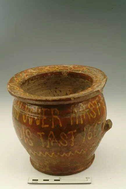 Ancient pottery jar with inscriptions and a handle, showing visible signs of aging and wear. scale measurement included at bottom.