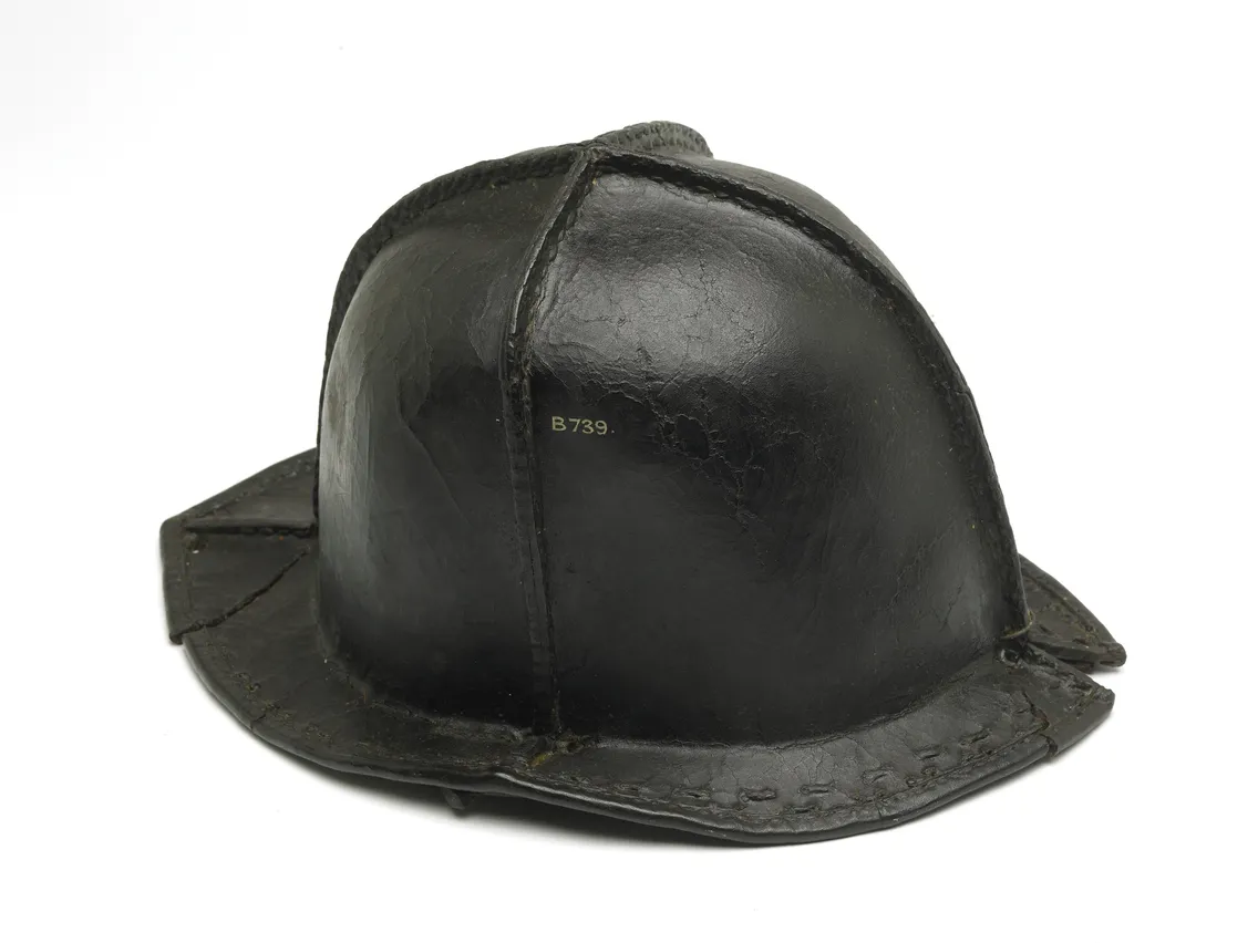 Vintage black leather firefighter helmet against a white background, showing signs of wear and age.