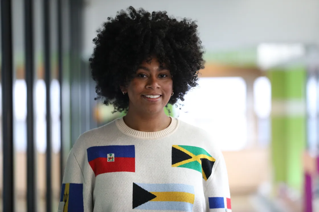A smiling Black woman standing in a corridor with green in the background.