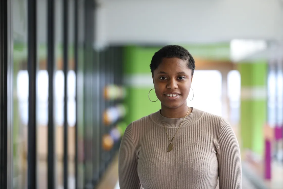 A smiling Black woman with gold hoop earrings standing in a corridor.