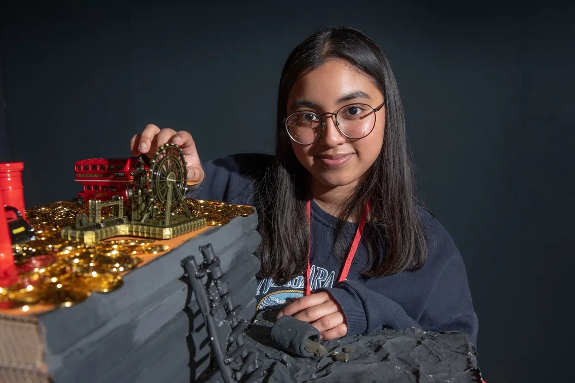 A person with glasses, wearing a dark shirt and red lanyard, interacts with a detailed mechanical model.