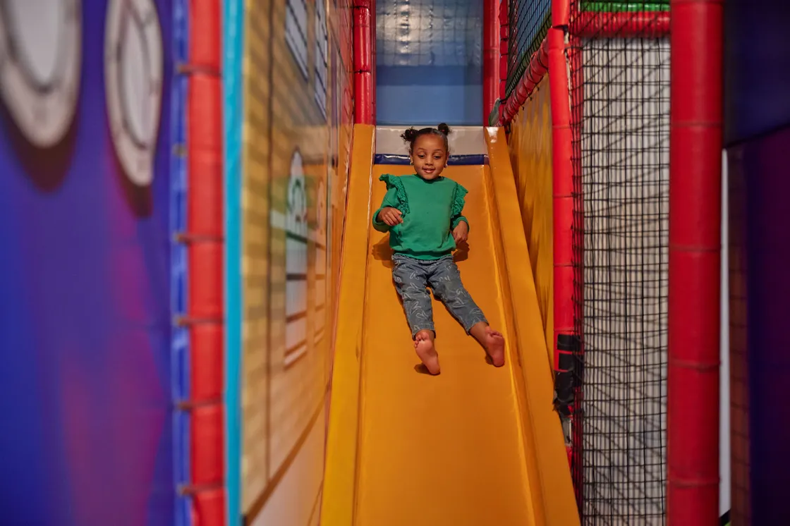 A smiling girl sliding down an orange slide
