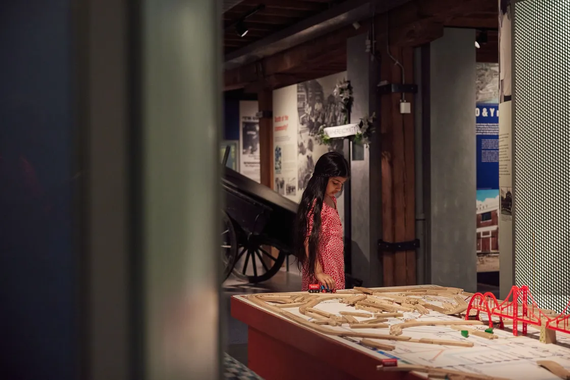 A girl alone pushing a red train along a train table
