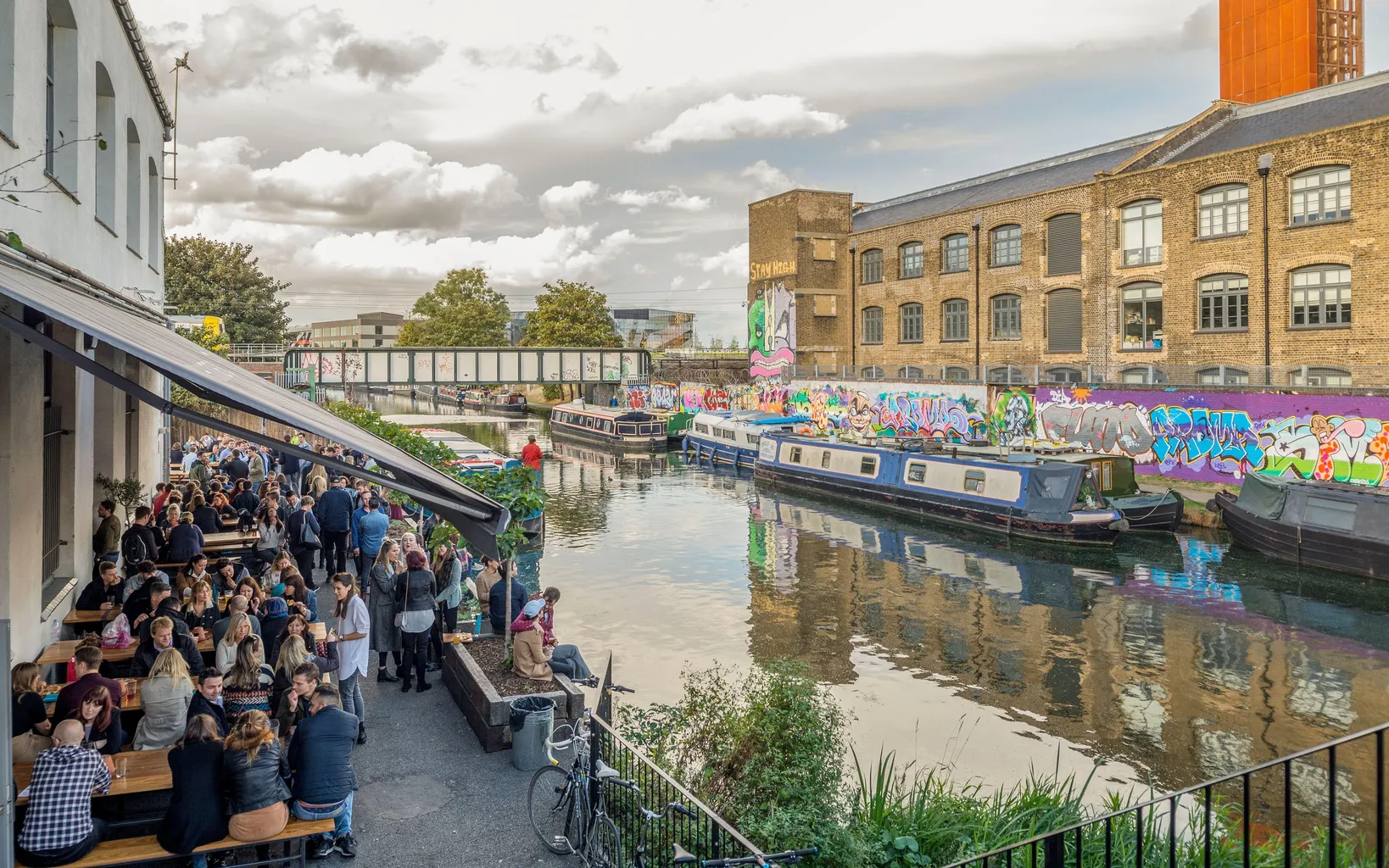 Groups of young hipsters socialise on a riverside bar and restaurant terrace on the bank of the river lea in Hackney Wick, East London, uk