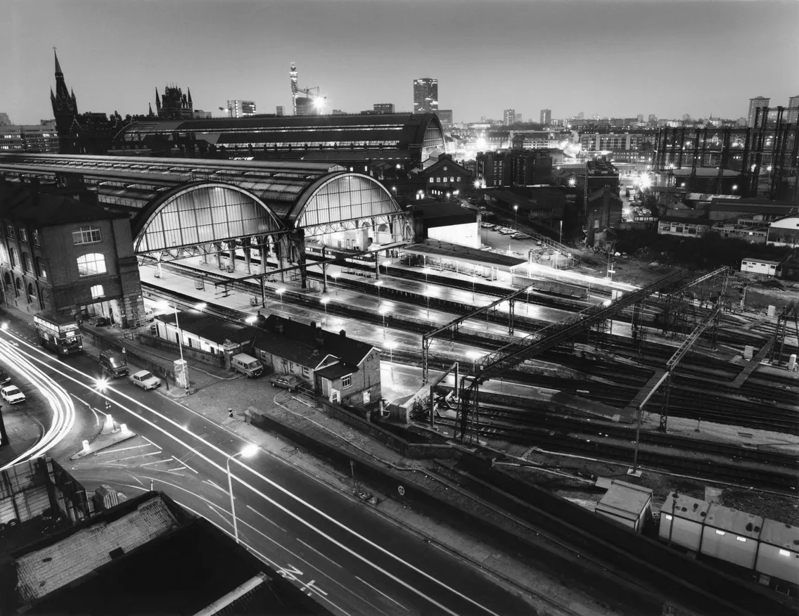 Nighttime view of a city train station with illuminated tracks and surrounding urban landscape.