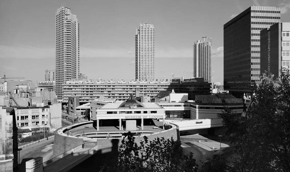 Black and white image of a cityscape featuring modernist buildings, with three tall tower blocks and the London Museum in the foreground.