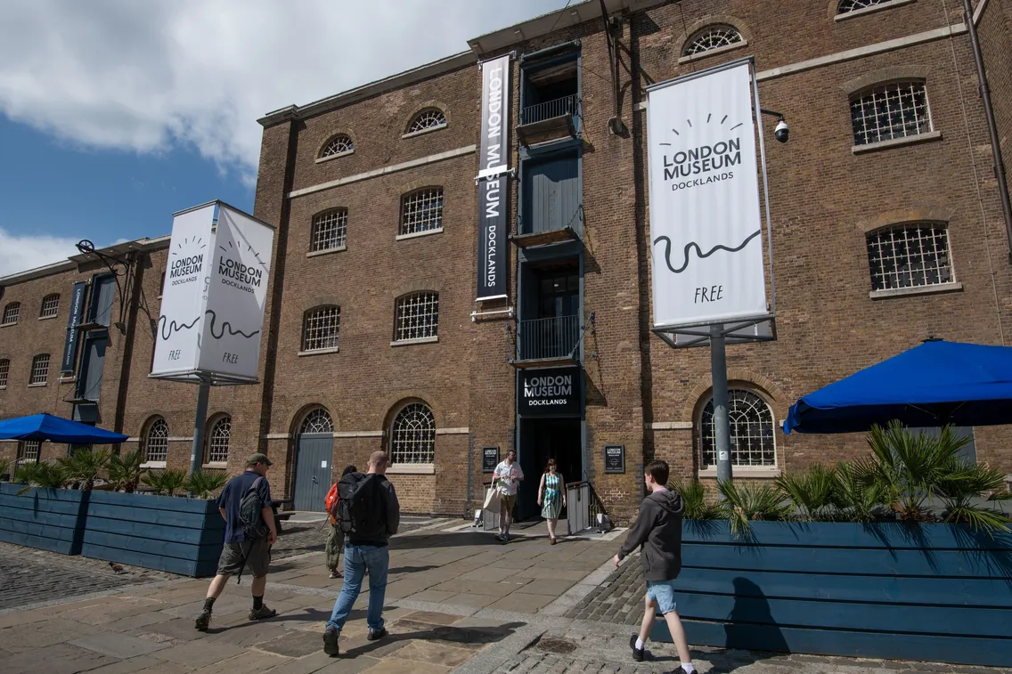 Exterior view of the London Museum Docklands with visitors walking nearby on a sunny day.