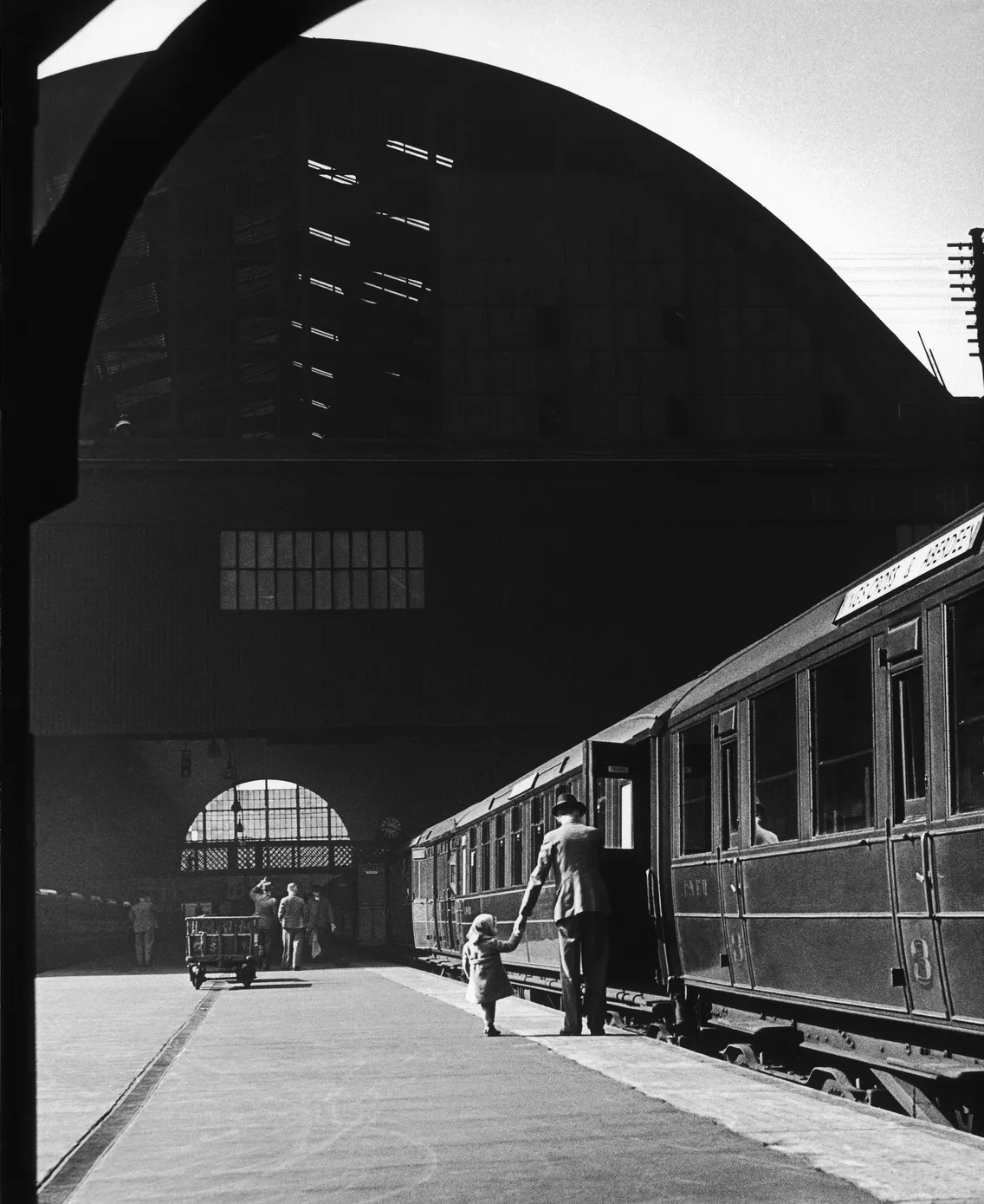 A man holds the hand of a child on a station platform next to a train.
