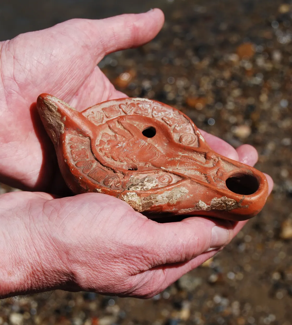 A person holding an old Roman lamp in their hand against the background of a beach.