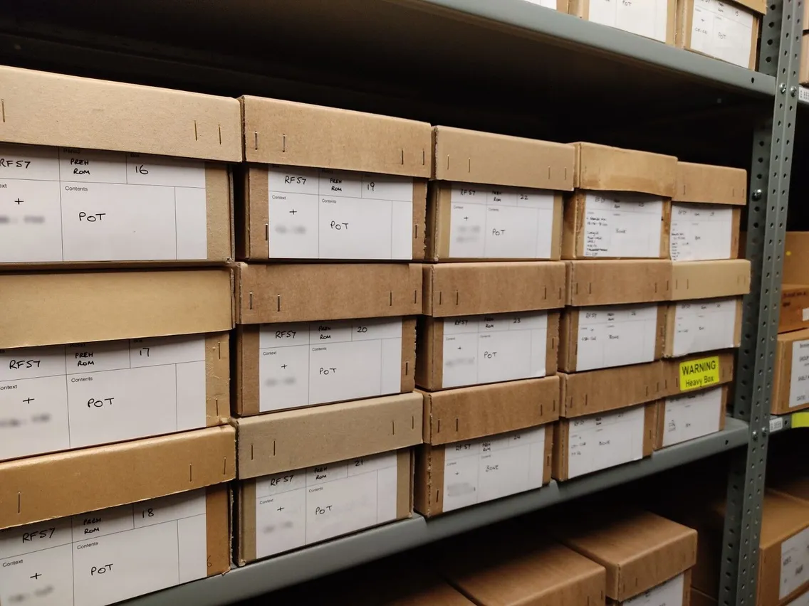Shelves filled with cardboard archive boxes, each labeled and sorted by category, in a storage room.