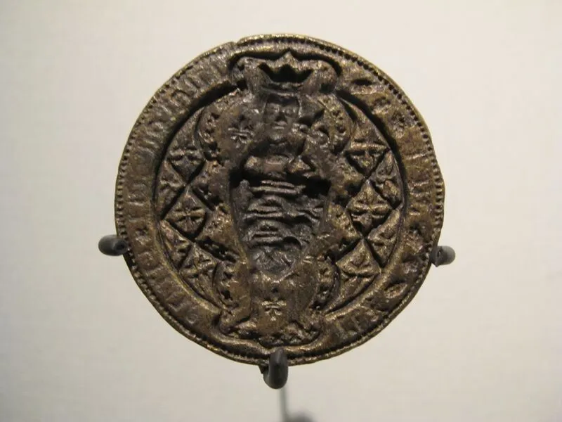 Ancient circular bronze shield boss featuring intricate designs and four mounting rivets, displayed against a grey background.