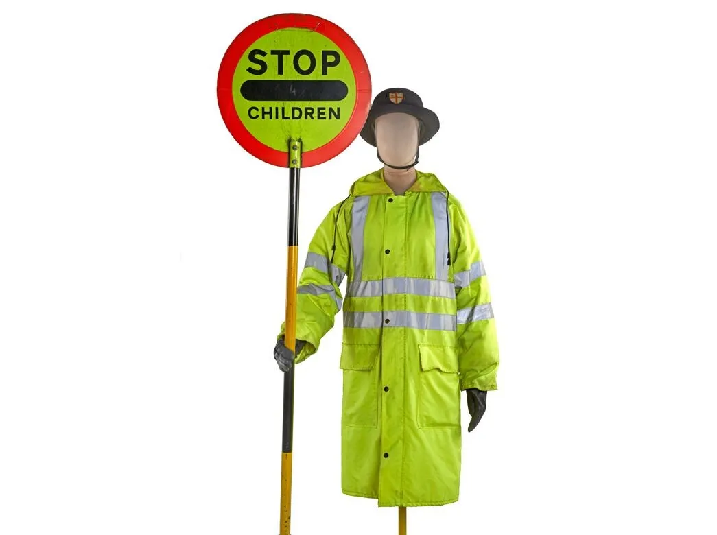 A mannequin dressed in a high-visibility jacket and gloves holds a "STOP CHILDREN" sign.