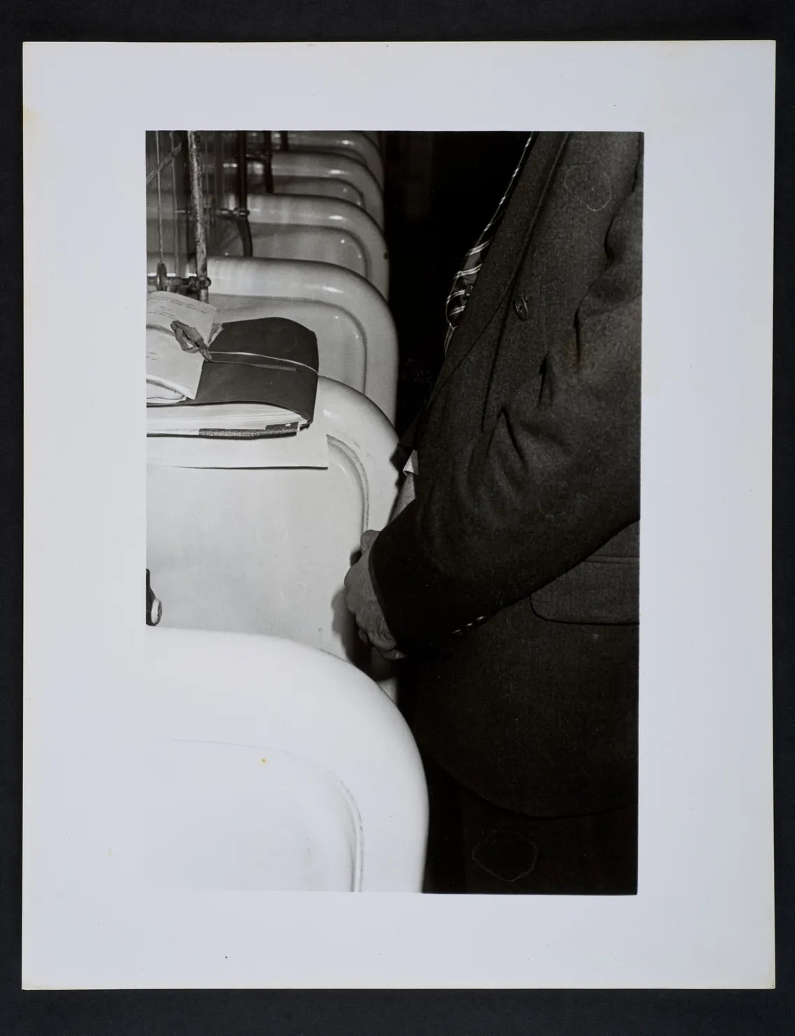 A person stands in front of a row of urinals in a restroom. The image captures only the waist and upper legs, with the focus on the first urinal in the row.