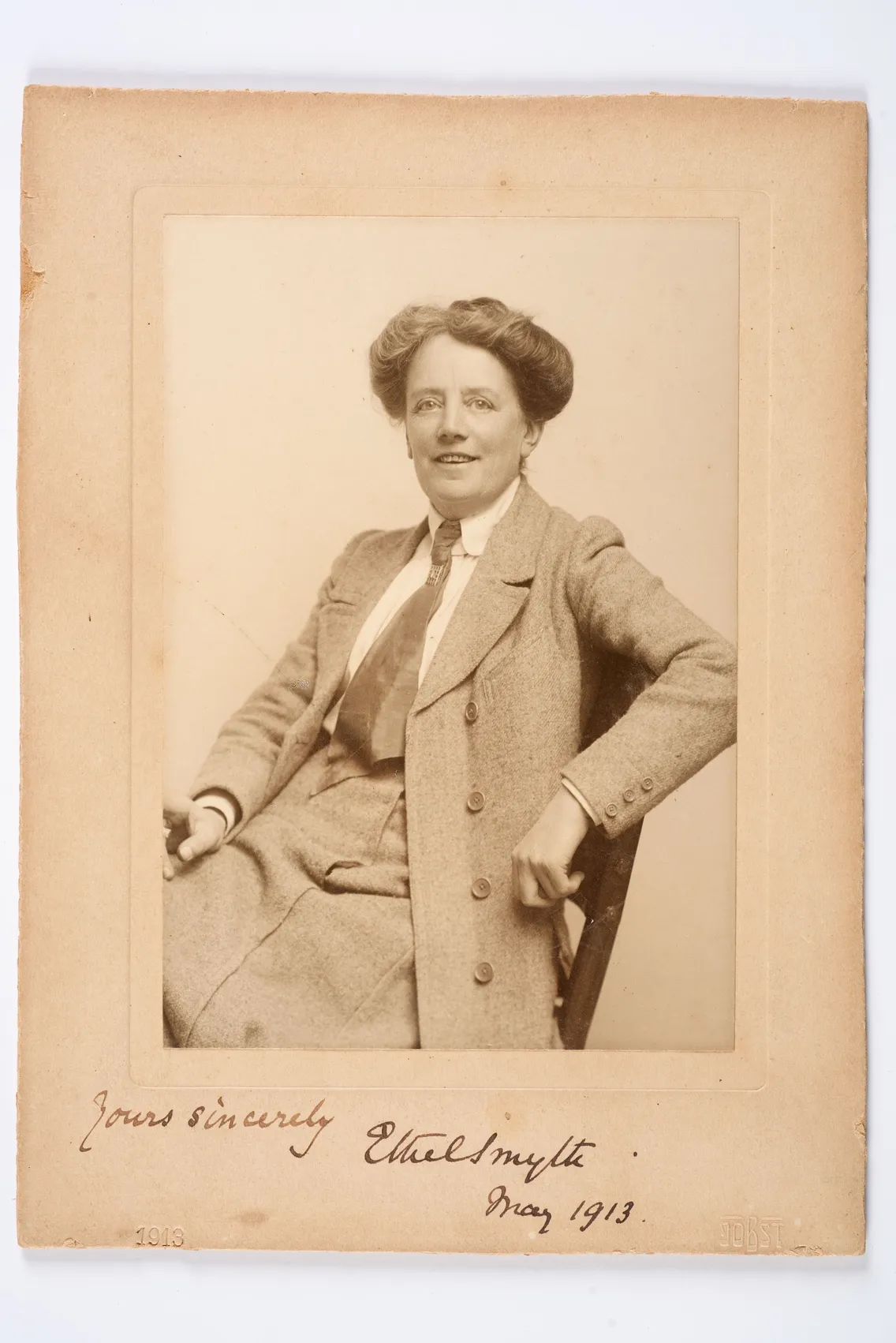 Vintage sepia-toned photograph of a person seated in a chair, dressed in a formal suit, looking directly at the camera, signed "yours sincerely ethel smyth may 1913.