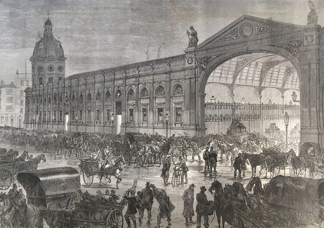A crowded 19th-century market with horse-drawn carriages, people, and luggage. The station has an ornate archway and extensive architectural details.