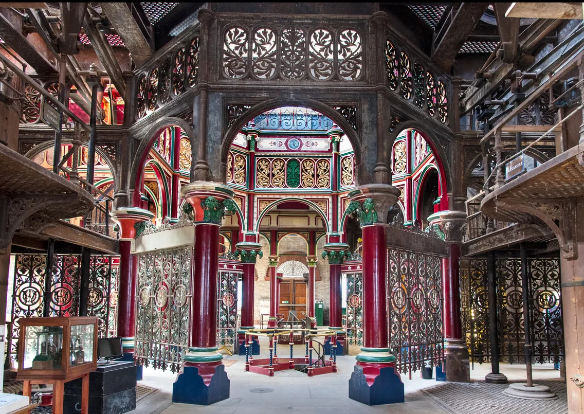 Interior of a historic library with intricate wrought iron columns, colorful decorative elements, and shelving units for books.