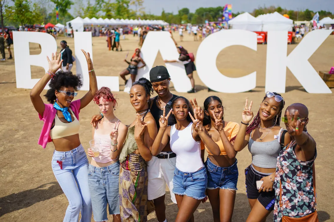 Group of smiling people posing in front of large white letters spelling "BLACK" at an outdoor event.